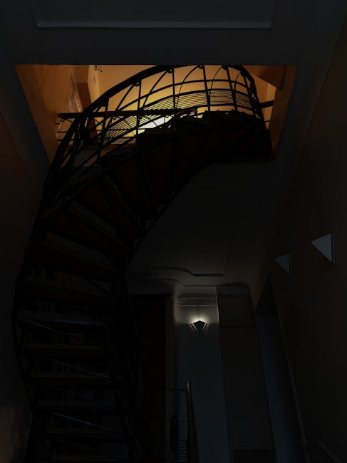 Inside a residential property at the top of a spiral staircase with metal railings and wooden steps, several cardboard boxes and wrapped items are arranged on the staircase landing. The staircase curv