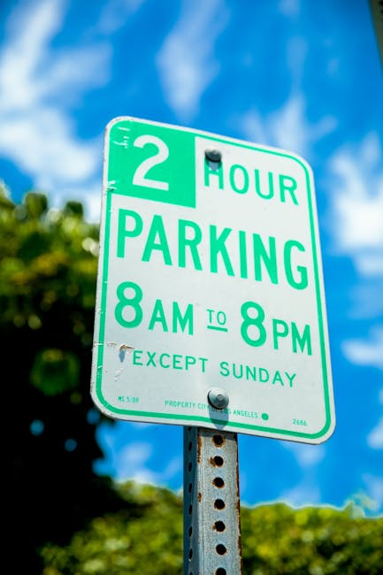 Close-up view of a green and white parking restriction sign attached to a metal pole, indicating a two-hour parking limit from 8 am to 8 pm, with an exception for Sundays. The sign is positioned outdo